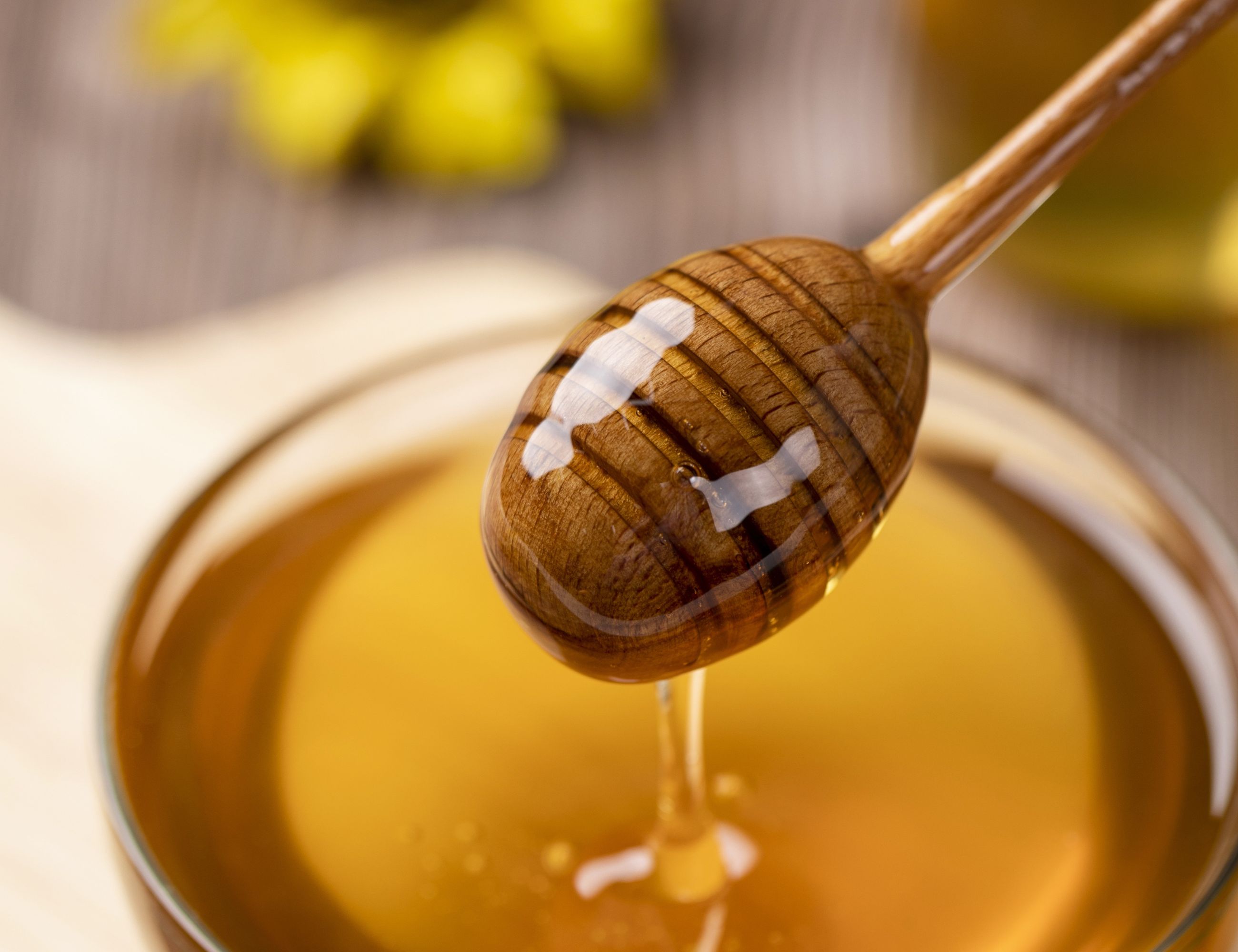 close up of golden honey in a dish with a wooden stir stick