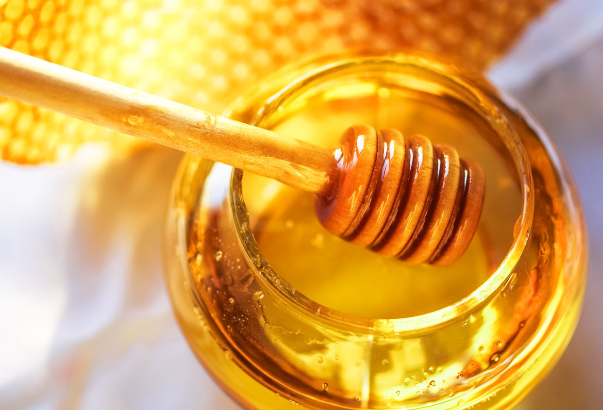 honey in a clear jar with a honey wooden spoon